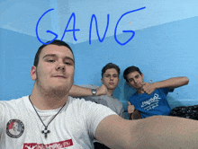 three young men are posing for a picture and the word gang is written on the wall behind them