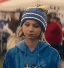 a young girl wearing a blue hoodie and a blue beanie is making a funny face .