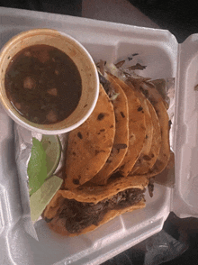 a styrofoam container filled with tacos and a cup of dipping sauce