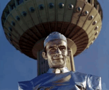 a statue of a man in a silver suit is in front of a very tall building