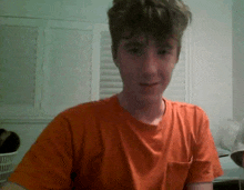 a young man wearing an orange t-shirt smiles for the camera