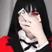 a woman with long black hair and red eyes is covering her face with her hands .