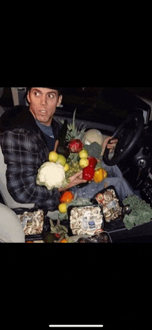 a man is sitting in a car holding a bunch of fruit and vegetables