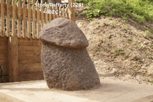 a large rock shaped like a penis sits in front of a wooden fence that says store / raferty ( 228 )