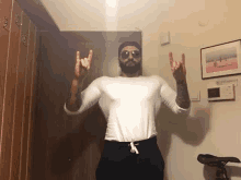 a man with a beard and sunglasses is making a horns sign with his hands in a hallway .