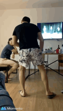 a man in shorts is dancing in front of a television and the word momento is on the bottom right