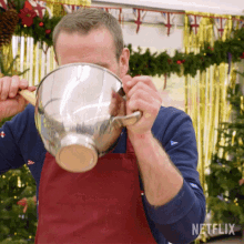 a man wearing a red apron is holding a metal bowl in front of his face with a netflix logo in the background