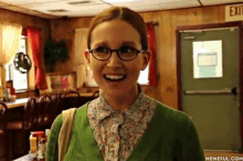 a woman wearing glasses and a green sweater is standing in a restaurant .