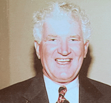 a man with curly hair wearing a suit and tie smiles for the camera