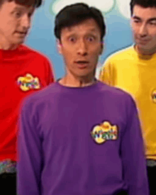 a man in a purple shirt is standing in front of two other men in red shirts .