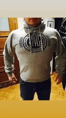 a man is standing in a room wearing a grey hoodie with the words rez style on it .