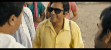 a man wearing sunglasses and a yellow shirt is standing in a crowd of people