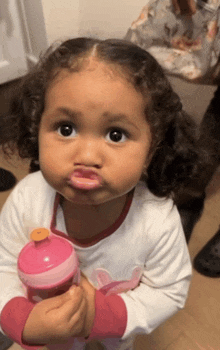 a little girl is holding a pink bottle and making a funny face