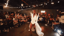 a woman in a white dress is dancing in front of a crowd with a sign that says coca cola on it