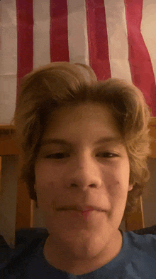 a young boy is making a funny face in front of a red white and blue flag