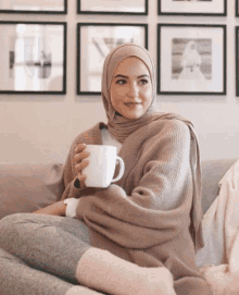 a woman in a hijab sits on a couch holding a cup