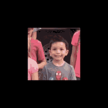 a young boy wearing a spiderman shirt is smiling for the camera while standing in a crowd of children .