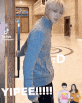 a man in a blue sweater is standing in front of a door holding a handle .
