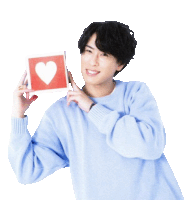 a young man in a blue sweater is holding a red card with a heart on it