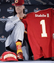 a man in a suit holding a red jersey with the number 1