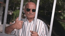 a man in sunglasses is giving a thumbs up behind bars .