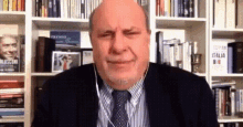 a bald man wearing a striped shirt and tie is sitting in front of a bookshelf with a book titled italia on it .