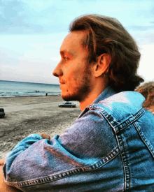 a man wearing a blue denim shirt looks out over the ocean