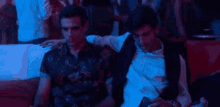 two men are sitting next to each other on a couch in a club and talking .