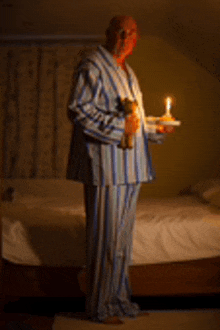 a man in striped pajamas holding a candle and a teddy bear