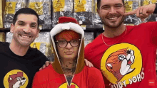 three men are posing for a picture in a store . one of the men is wearing a red shirt with a dog on it .