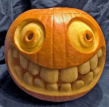 a pumpkin carved to look like a cartoon character with big teeth and big eyes is sitting on a blue cloth .