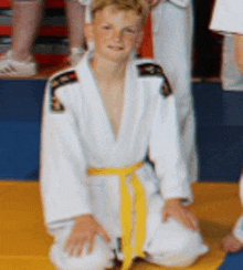 a young boy in a white karate uniform with a yellow belt sits on the floor