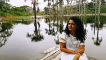 a woman in a white dress is sitting on a dock near a lake