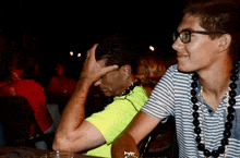 a man in a neon green shirt is covering his face while another man wearing glasses looks on