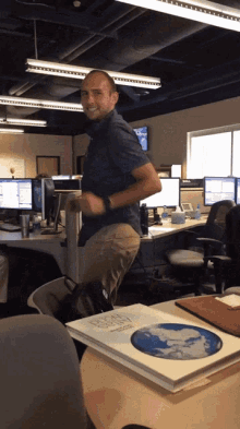 a man in a blue shirt is dancing in an office with a book on the desk that says earth science