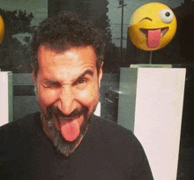 a man with a beard is making a funny face in front of a statue of an emoji .