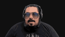 a man with a beard and sunglasses is wearing headphones and a black shirt .