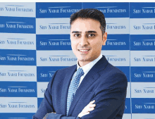 a man in a suit and tie stands in front of a wall that says shiv nadar foundation