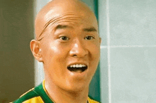 a bald man wearing a yellow and green shirt is making a funny face with his mouth open .