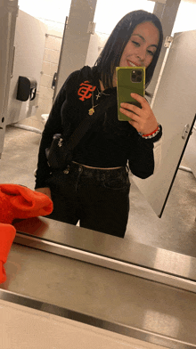 a woman taking a selfie in a bathroom with a san francisco giants shirt on