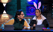 a man and a woman are sitting at a table in front of a neon sign that says on the air