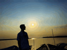 a man in a white shirt stands in front of a body of water at sunset