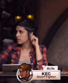 a woman in a plaid shirt sits at a table with a sign that says kec dwarf fighter