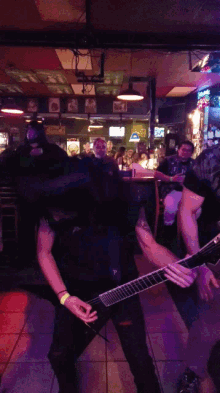 a man playing a guitar in front of a crowd in a bar with a neon sign that says ' bud light ' on it