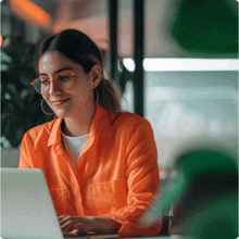 a woman in an orange shirt is using a laptop computer