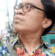 a man wearing glasses and a floral shirt looks up at the sky