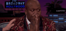 a man is covering his mouth with his hands in front of a broadway hollywood sign