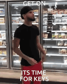 a man in a black shirt and red shorts stands in front of a refrigerator with the words get on its time for keys