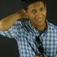 a man in a blue and white checkered shirt is holding sunglasses and smiling .