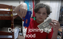 a boy is holding a toy gun and a dollar bill with the words day 1 of joining the hood above him